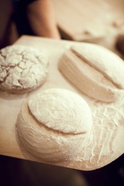 Tahta kesme tahtasının üzerinde üç somun ekmek duruyor. Farklı şekillerde ve büyüklükte somun ekmeği yapıyorlar. Doğa, yemek, diyet, yemek pişirme, fırın, yemek tarifleri,.