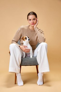 Kendinden geçmiş genç kız, mutlu ve neşeli sahibi en sevdiği evcil hayvanıyla takılıyor bej arka planda saf Jack Russel Terrier. Hayvan, hayvan sever, arkadaşlık, yaşam tarzı, arkadaşlık kavramı.