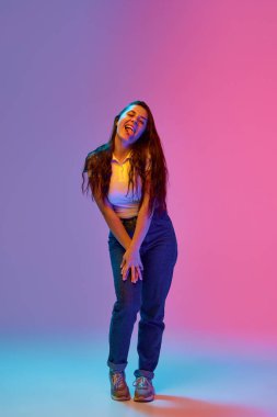 Full-length portrait of positive and funny young brunette woman with freckles grimacing against gradient background in neon light. Concept of beauty and youth, human emotions, self-expression. Ad