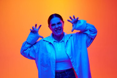 Negative emotions. Irritated young woman, girl expressively showing emotion of rage angry against gradient studio background in blue neon light. Concept of youth and beauty, human emotions. Ad