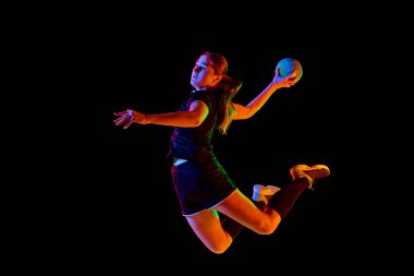 Fit, young, competitive female handball player demonstrating throwing techniques against black background in neon light. Concept of professional sport, movement, dynamic, workout, championship 2024
