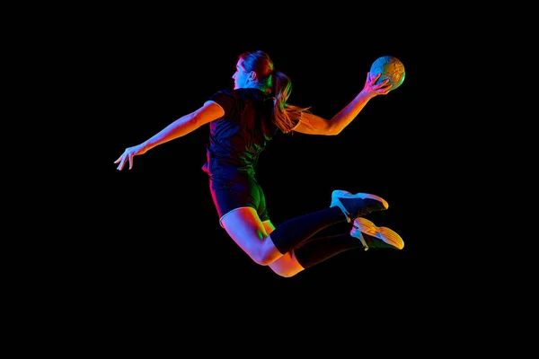 Young female handball athlete practicing throws and receptions against black background in neon light. Energetic and focused training session. Concept of professional sport, dynamic, championship. Ad