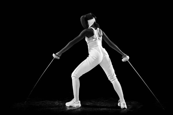 Dual-blade mastery portrait of female fencing maestro, confidently posing with two swords against black studio background. Artistry and precision of sport Concept of professional sport, championship.