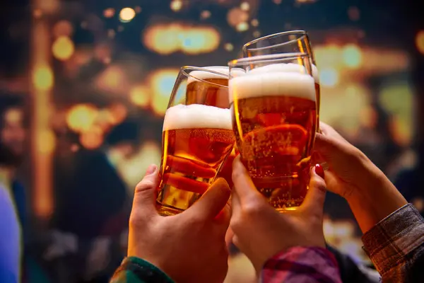 Close up shot of unrecognizable group of friends saying toasts and drinking beer and clinking glasses in bar while watching match. Concept of Oktoberfest, party, celebration, national traditions.