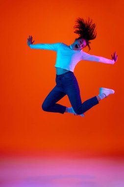 Neon ışıkta pembe-turuncu arka planda mutluluk ve sevinç içinde zıplayan genç kadının tam boy portresi. Kendini ifade etme kavramı, güzellik ve moda, enerji. Ad