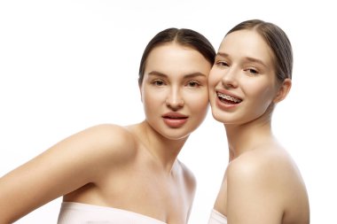 Doğal makyajlı iki kadın, beyaz stüdyo arka planında açık tenlerini ve narin güzelliklerini ön plana çıkarıyor. Doğal güzellik insanları, gençlik, organik kozmetik, tedavi kavramı. Ad