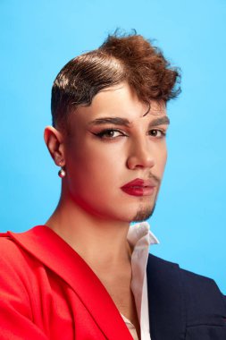 Kıtlık ve erkeksi makyajlı bir model portresi mavi arka planda kameraya bakıyor. Avantaj-Garde ifadesi. Kendini ifade etme, seçme özgürlüğü, cinsiyet eşitliği kavramı. Ad