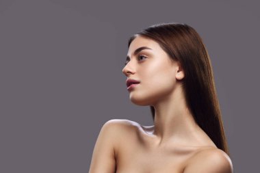 Side profile of a young woman with sleek hair and bare shoulders, presenting clean, elegant look against grey background. Concept of haircare, strong, healthy hair and natural shine. Ad clipart