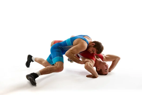 Two young athlete man, skilled wrestlers in red and blue uniform wrestling in motion against white studio background. Concept of sport, mixed martial arts, active lifestyle, movement.