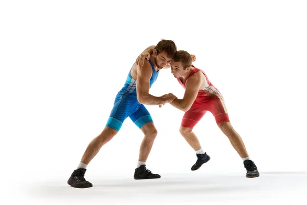 Young athlete man, wrestlers in blue and red uniform hand wrestling in motion against white studio background. Concept of sport, mixed martial arts, active lifestyle, movement. Ad