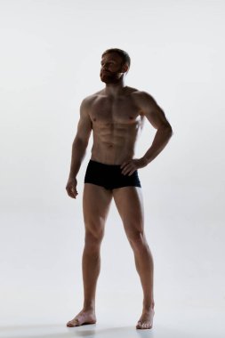 Mükemmel vücut şekilleri olan beyaz arka planda iç çamaşırlarıyla poz veren çekici genç bir adamın tam boy portresi. Doğal güzellik kavramı, estetik beden, erkek sağlığı, erkeklik..