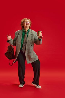 Cuma havası. Aşırı neşeli son sınıf hanımı, şık giyinmiş, kırmızı stüdyo arka planında dans ediyor. İş anlayışı, modaya uygun yaşlı yetişkinler, modern yaşamın aktif yaşlıları.