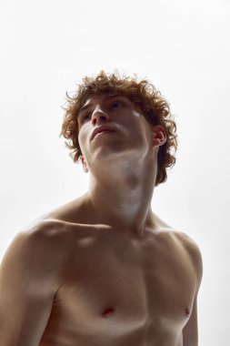 Çağdaş sanat. Beyaz stüdyo arka planında çıplak vücut pozu veren çekici, güneşli genç bir adamın portresi. Modern bale, sanat ve güzellik, ilham, zarafet konsepti.