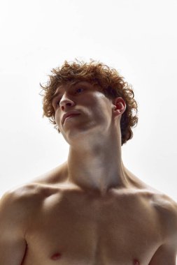 Çağdaş sanat. Beyaz stüdyo arka planında çıplak omuzlarıyla poz veren kıvırcık saçlı genç atletik adamın portresi. Modern bale, sanat ve güzellik, ilham, zarafet konsepti.