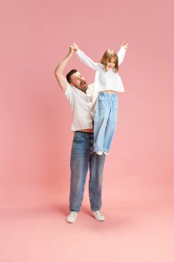 Babam ve ben. Pembe pastel arka planda kollarını kaldırmış çocuğu tutan adamın tam boy portresi. Uluslararası Mutluluk Günü kavramı, çocukluk ve ebeveynlik, olumlu duygular. Ad