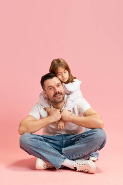 Pembe pastel arka planda sırtüstü uzanmış çocuk ile bağdaş kurmuş oturan memnun bir adam. Uluslararası Mutluluk Günü kavramı, çocukluk ve ebeveynlik, olumlu duygular. Ad