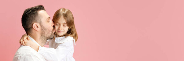 Баннер. Отец целует свою милую маленькую дочь на розовом пастельном фоне с негативным пространством для вставки текста. Концепция Международного дня счастья, детства и родительства, положительная. Объявление