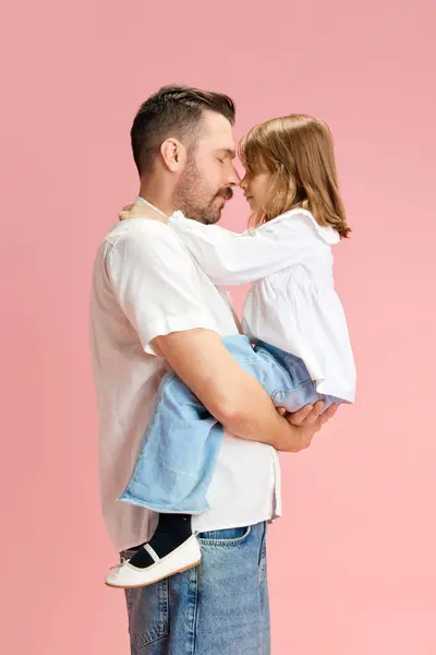 Calm. Portrait of father holds on hands and hugs his little daughter against pink pastel background. Concept of International Day of Happiness, childhood and parenthood, positive emotions. Ad