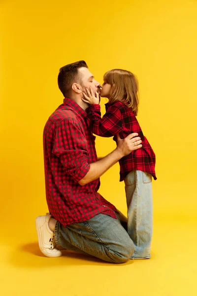 Little kid, girl kissing with love her dad. The best father in world and his lovely daughter against vivid yellow background. Concept of International Day of Happiness, childhood and parenthood. Ad