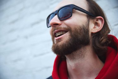 Şehir manzaralarına bakarken diş telleriyle gülümseyen genç sakallı adamın yakın fotoğrafını çek. Sağlık ve ilaç kavramı, güzellik, yaşam tarzı, olumlu, duygular, boş zaman.