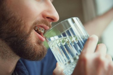 Kesilmiş portre. Diş teli takmış genç sakallı adamın yakın plan fotoğrafını çek. İçme suyu. Su dengesi. Diyet ve beslenme Güzellik ve ilaç kavramı, sağlık, yaşam tarzı.