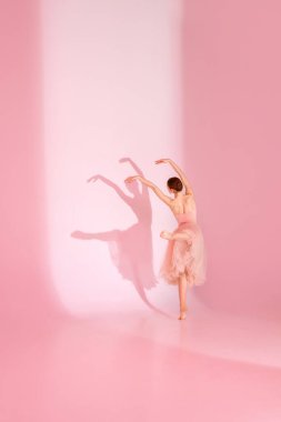 Huzur Dansı. Genç bir kadının dinamik portresi, pembe mayo ve etekli balerin gölgesi ile pastel pembe arka planda çıplak ayakla poz veriyor. Zarafet kavramı, bale, güzellik.