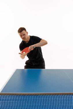 Siyah spor üniformalı adam masa tenisi oynuyor. Beyazlara karşı mükemmel servis yapmak için topa odaklanmış. Profesyonel spor, şampiyonluk, turnuva, zafer ve kazanma kavramı. Ad