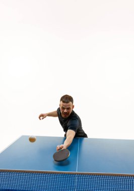 Atletik, masa tenisçisinin beyaz stüdyo arka planına karşı topa vuruşunun dinamik çekimi. Profesyonel spor, şampiyonluk, turnuva, eylem, güç ve güç kavramı.