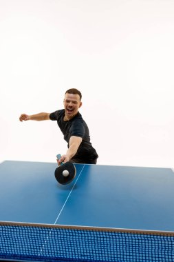 Genç bir adam, masa tenisi yarışmacısı. Beyazların arka planına karşı oynadığı yarışma sırasında salıncakta. Profesyonel spor, şampiyonluk, turnuva, eylem, güç ve güç kavramı.