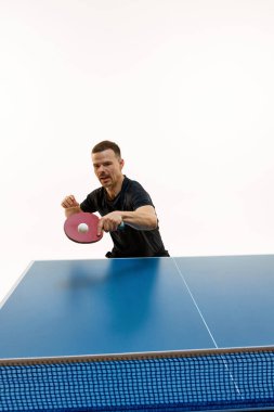 Yoğun masa tenisi rallisi. Beyaz arka planda hareket eden genç bir oyuncunun dinamik portresi. Profesyonel spor, şampiyonluk, turnuva, aksiyon, güç ve güç kavramı. Boşluğu kopyala.