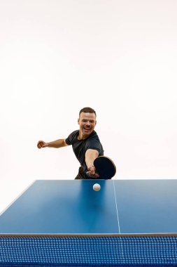 Rekabetçi ve pozitif genç bir adam, masa tenisi oyuncusu. Beyazların arka planına karşı sahada topa vurmakta kararlı. Profesyonel spor, dinamik ve enerji kavramı, şampiyonluk, turnuva.