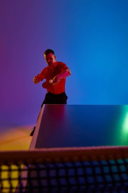 Genç adam, salıncakta sallanan masa tenisi yarışmacısı neon ışıkta arka plandaki değişime karşı mücadele ediyor. Dinamik jel portresi. Profesyonel spor anlayışı, sağlıklı yaşam tarzı. Ad