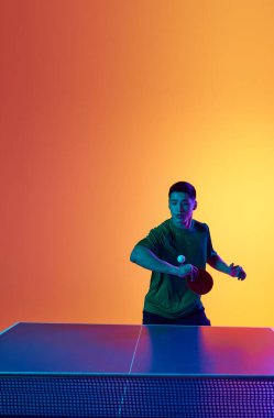 Masa tenisi anı, neon ışıkta sıcak sarı gradyan arka planda yakalanır. Dinamik jel portresi. Profesyonel spor anlayışı, sağlıklı yaşam tarzı ve eğlence. Ad