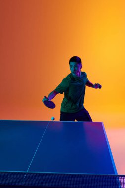 Kendine güvenen ve Asyalı masa tenisi oyuncusu neon ışığın sıcak sarı gradyan arka plana odaklanmış portresi. Dinamik jel portresi. Profesyonel spor kavramı, maç, gol. Ad