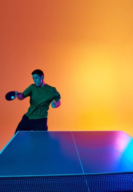 Asyalı atlet, ping pong oyuncusu antrenmanı topa neon ışıkta vuruyor sıcak sarı eğimli arka planda. Dinamik jel portresi. Profesyonel spor, güç ve güç kavramı. Ad