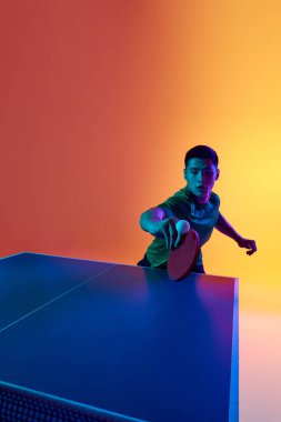 Yoğunlaştırılmış Asyalı erkek oyuncu ile pinpon oyunu neon ışıklarıyla sıcak sarı eğimli arka plana karşı. Dinamik jel portresi. Profesyonel spor anlayışı, sağlıklı yaşam tarzı ve eğlence. Ad