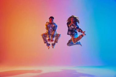 Enerjik pozitif çift, dansçıların neon renkli ışıkla zıplaması havada asılı olarak gradyan arkaplana karşı. Hareket kavramı, enerji, dans savaşları. Dinamik jel portresi