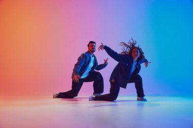 İki genç dansçı, neon ışıklı, filtreli gradyan stüdyo arkaplanına karşı dans eğitimi veriyor. Gençlik kültürü, müzik, yaşam tarzı, tarz ve moda, eylem kavramı. Jel portresi.