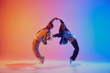 Genç dans ikilisinin el ele tutuşup neon ışıkta arka planda dans edişinin dinamik çekimi. Gençlik kültürü, müzik, yaşam tarzı, tarz ve moda, eylem kavramı. Jel portresi.