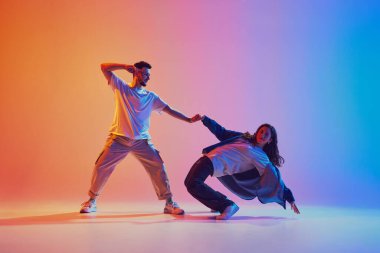 Neon ışığı ve filtresiyle, arka plandaki gradyan stüdyoda dans eden kadın ve erkeğin dinamik portresi. Performans. Gençlik kültürü, müzik, yaşam tarzı, eylem kavramı. Jel portresi.