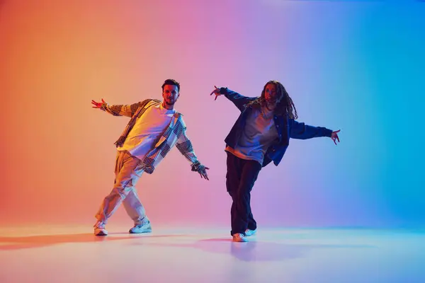 Two dancers, man and woman dancing in motion against gradient studio background. Dynamic movement. Concept of youth culture, music, lifestyle, style and fashion, action. Gel portrait.