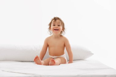 Mutlu bebek, ıslak saçlı küçük kız, beyaz stüdyo arka planında yumuşak, beyaz bir yatak örtüsünde oturuyor. Çocukluk kavramı, annelik, yaşam, doğum. İlan için alanı kopyala