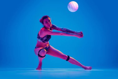 Spor giyimli, dinamik atletik, formda bir kadın, pembe neon ışıkta, gradyan mavi arka planda alçaktan hareket ediyor. Spor anlayışı, hareket, aktif, sağlıklı yaşam tarzı, güç, güç.