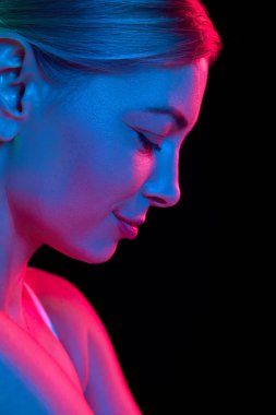 Genç ve çekici bir kadının renkli neon ışıklarıyla siyah stüdyo geçmişine bakarken çekilmiş yakın bir fotoğrafı. Doğal güzellik kavramı, yaşlanma karşıtı, kozmetik bilimi, kadın sağlığı. Ad