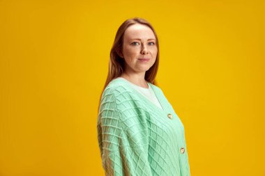 Zevk ve mutluluk. Güzel gülüşlü, sarı stüdyo arka planına bakan genç ve çekici kızıl saçlı kadın. Güzellik ve moda kavramı, kendini ifade etme, insani duygular. Ad