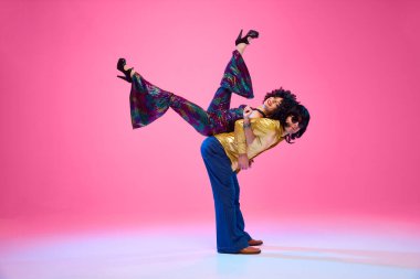 Dansın ritmine. Yetenekli bir çift, dinamik disko pozlarında dans partnerleri gradyan pembe stüdyo arka planına karşı. Amerikan kültürü kavramı, 1970 'ler, 1980' ler moda, müzik, çağların karşılaştırmaları..