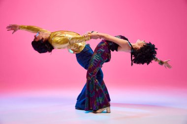 70 'lerin yankıları. Dans ikilisi, kadın ve erkek dansçılar eski moda kıyafetleriyle gradyan pembe stüdyo geçmişine karşı poz veriyorlar. Amerikan kültürü kavramı, 1970 'ler, 1980' ler moda, müzik, sanat, hobi.