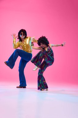 Coşkulu disko dansçıları, 70 'li yaşlarda erkek ve kadın renkli giyinmiş gradyan pembe stüdyo arka planında dans ediyorlar. Amerikan kültürü, 1970 'ler, 1980' ler moda, müzik, dönemin karşılaştırmaları .