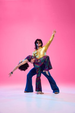 Disko ikilisi dansın ortasında, İspanyol paça giyen bir adam gradyan pembe stüdyo arka planına karşı partner kaldırıyor. Sanatçılar hareket halinde. Amerikan kültürü kavramı, 1970 'ler, 1980' ler moda, müzik, çağların karşılaştırmaları..