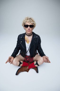 Deri ceketli ve etekli adam meditasyon yapıyor, punk modayla geleneksel İskoç modasını birleştirerek gri stüdyo arka planına karşı çıkıyor. Moda birleşimi, sanat fotoğrafçılığı, tarz, kendini ifade etme kavramı. Ad